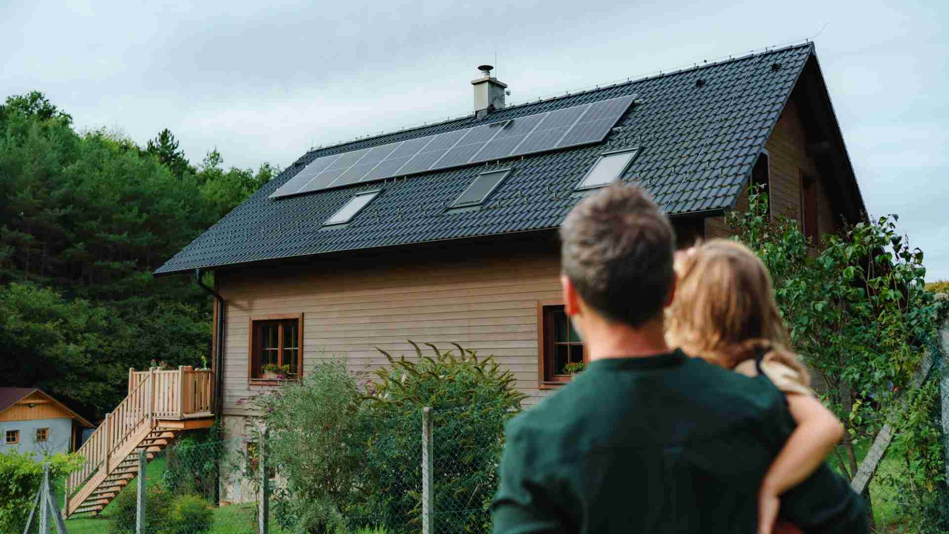 Photo d'un homme et de sa fille qui regarde leur maison avec des panneaux photovoltaïques